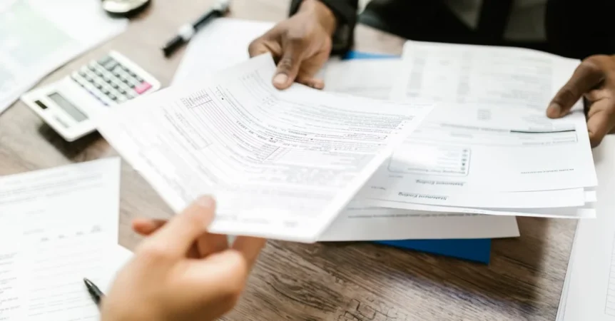 Two people reviewing tax documents and financial statements at wooden desk with calculator.