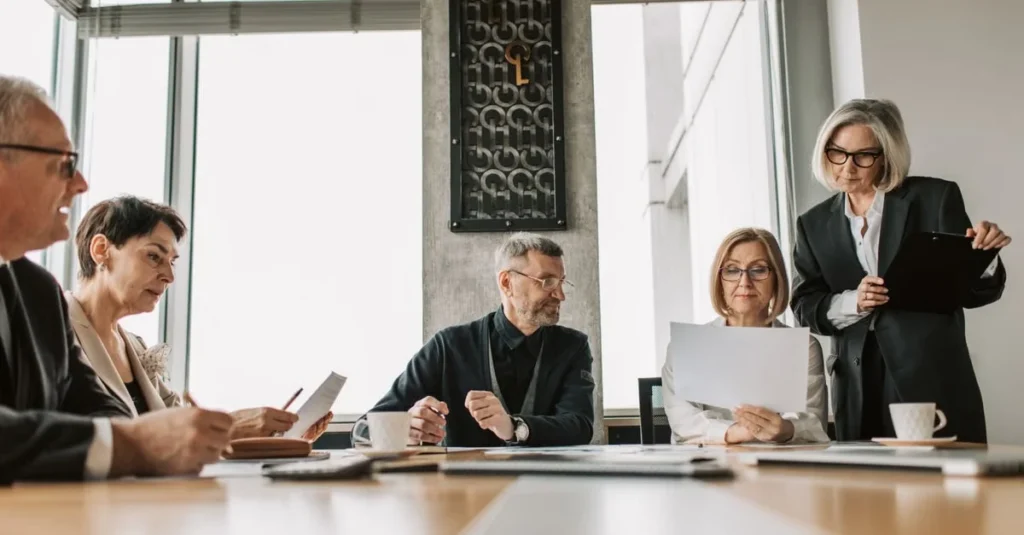 High net worth estate planning attorney leading boardroom meeting with diverse clients and colleagues at conference table.