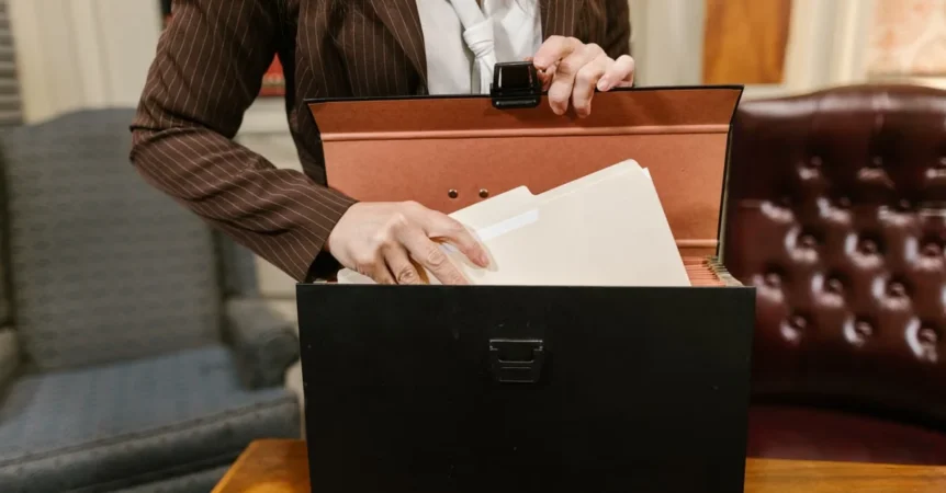 Professional woman organizing business sale documents in filing box during transaction preparation.