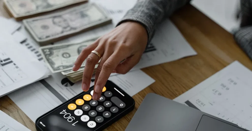 Hand using black calculator on desk with cash and financial documents for tax planning calculations.