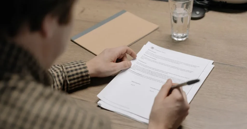 Person reviewing probate requirements document at desk with pen and water glass.