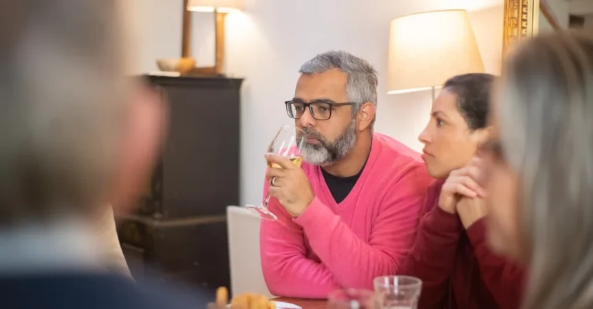 Man in pink shirt discussing estate planning legacy with group around table in warm, intimate home setting.